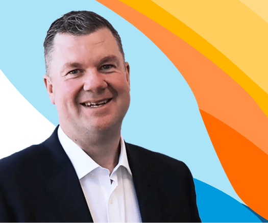 Headshot of a smiling man in a dark suit jacket against a blue and orange graphic background for an ai-powered ats & crm for recruitment agencies.