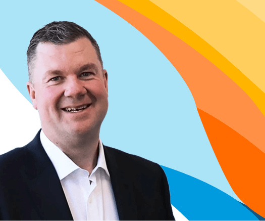 Headshot of a smiling man in a dark suit jacket against a blue and orange graphic background for an ai-powered ats & crm for recruitment agencies.