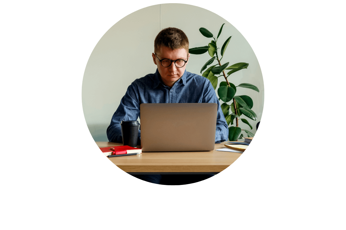 A man in glasses sits at a desk with a laptop, representing Bullhorn Workforce Management software.