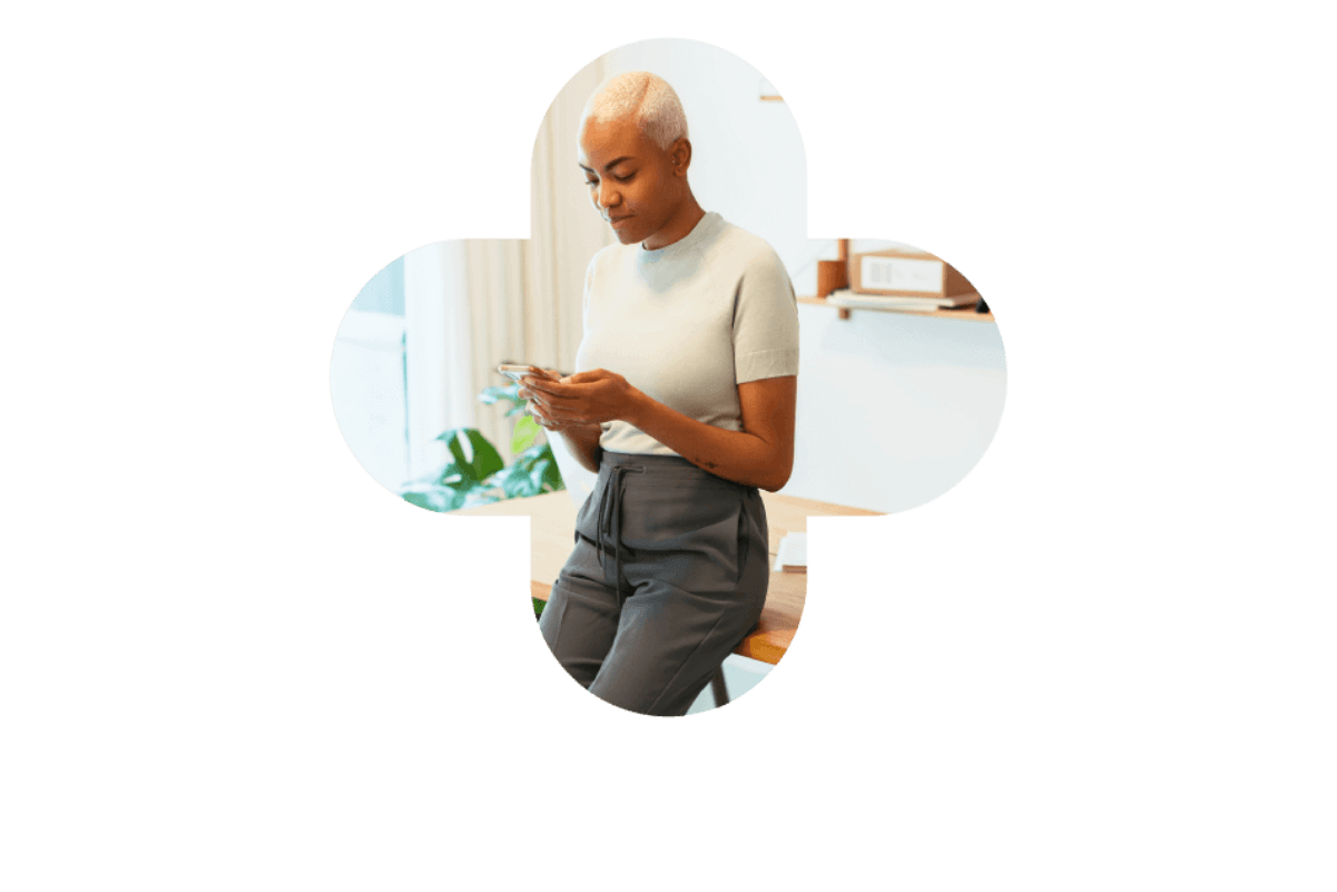 A woman in a white shirt and grey pants uses her phone, representing Bullhorn Workforce Management software.
